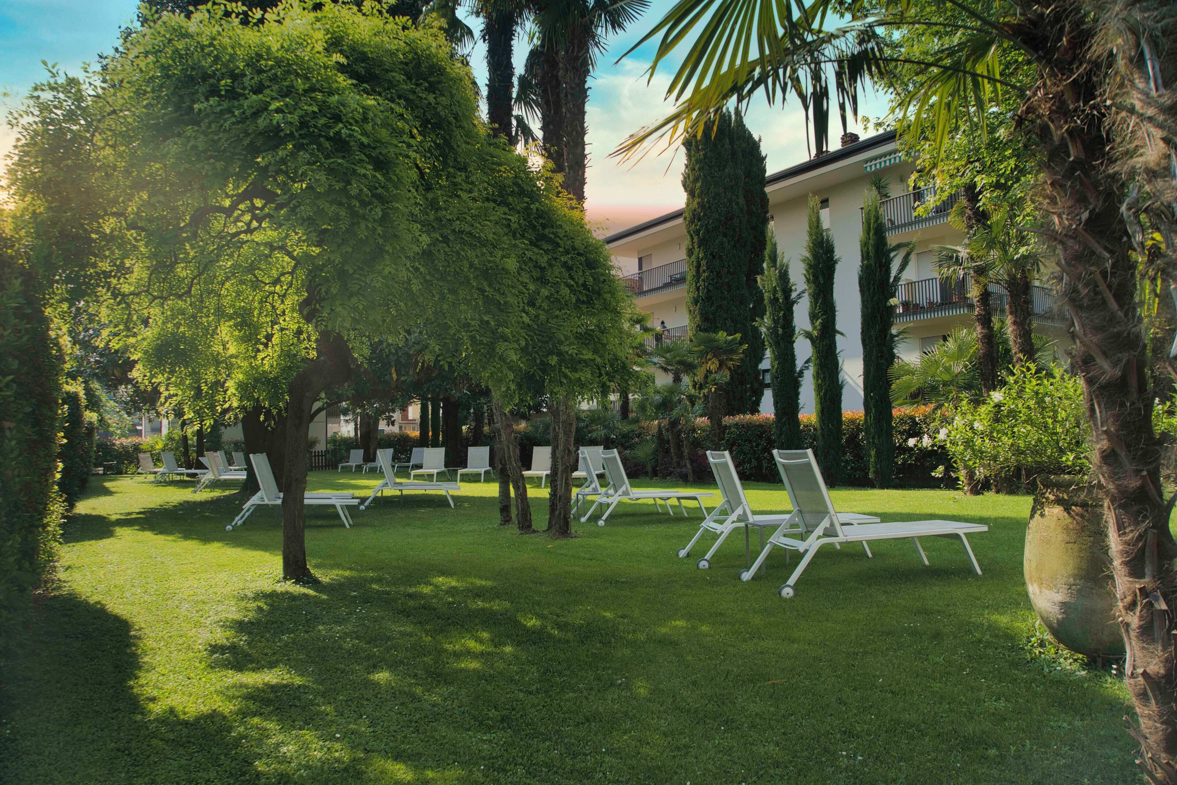 A courtyard with white lounge chairs, a large tree, and a building with balconies in the background.