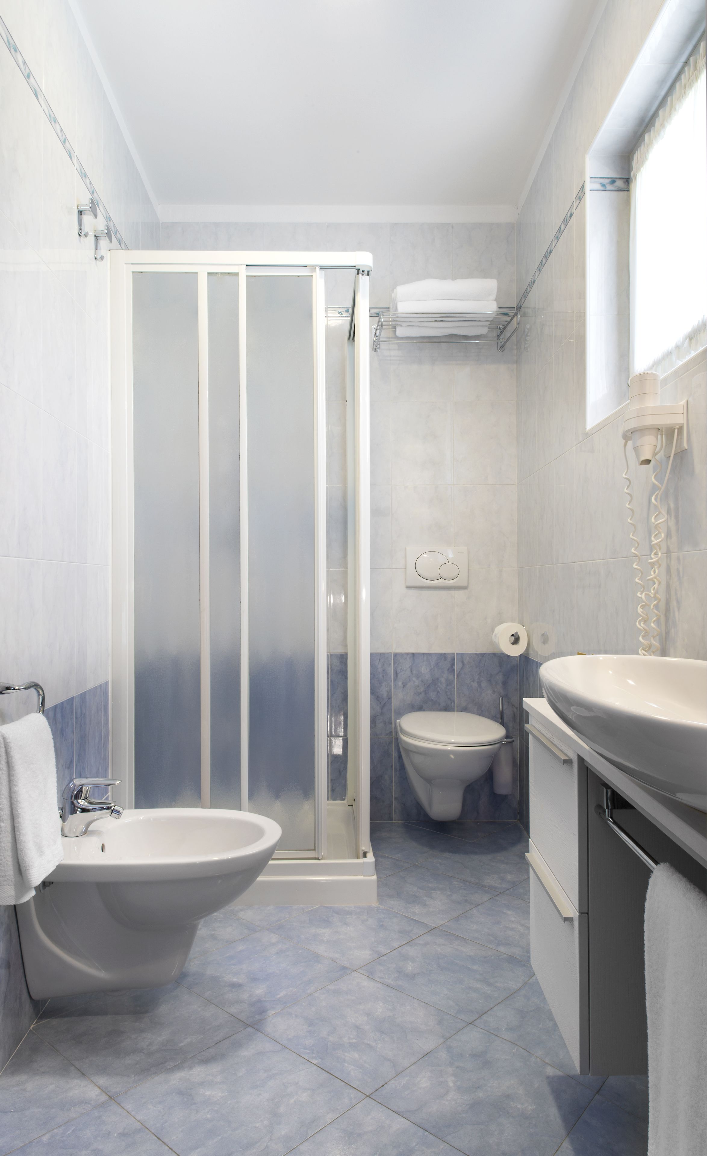 A bathroom with a shower enclosure, toilet, sink, and a towel rack.