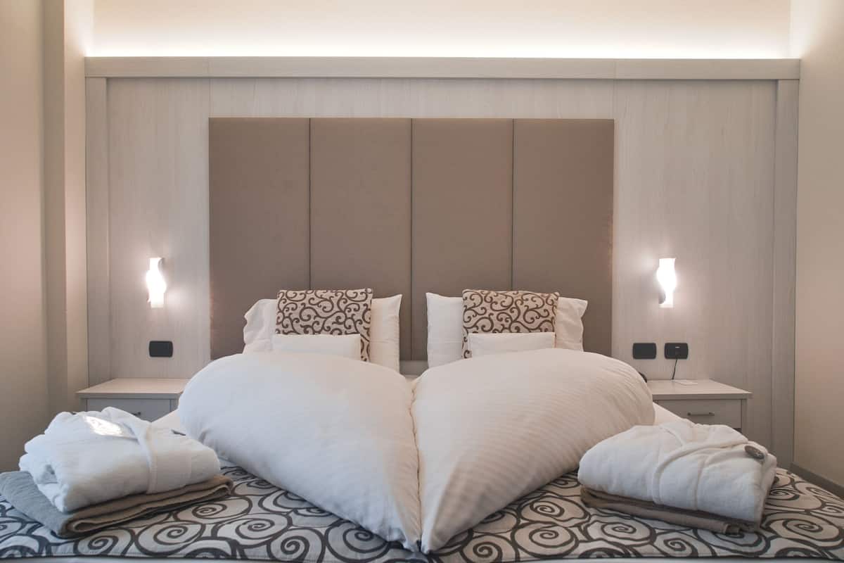 Una cama doble con almohadas con forma de corazón, dos mesitas de noche e iluminación para lectura en la pared.