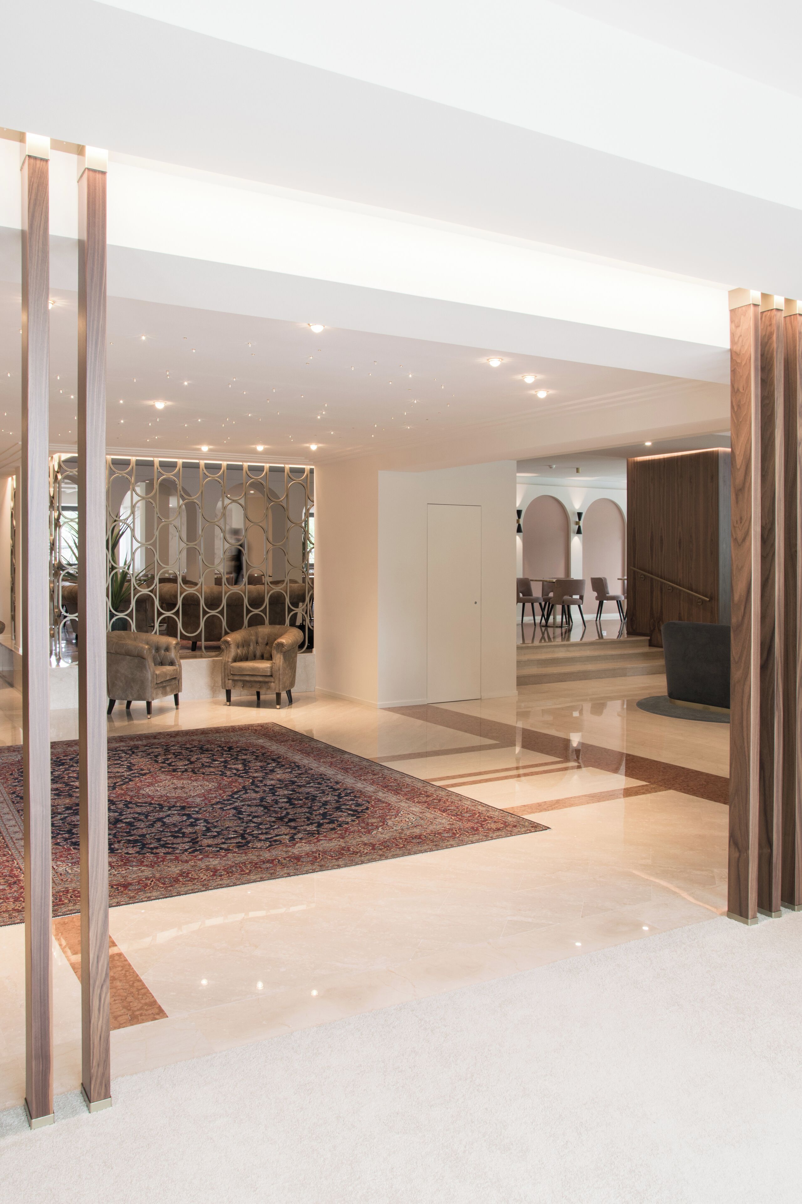 Una hall d'albergo moderna con un tappeto grande e decorato, un'area salotto con poltrone e una scala che conduce a un altro piano.