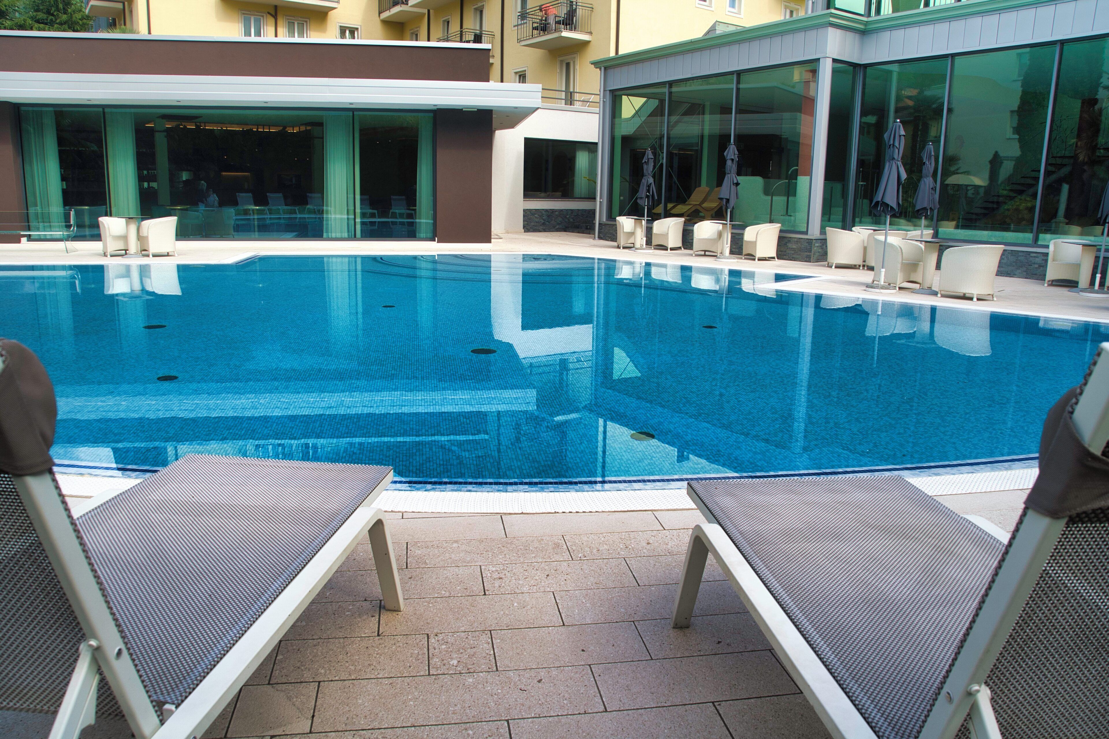 A swimming pool with lounge chairs and umbrellas, surrounded by a building with large windows.