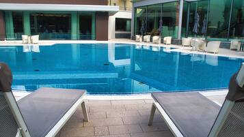 A swimming pool with lounge chairs and umbrellas, surrounded by a building with large windows.
