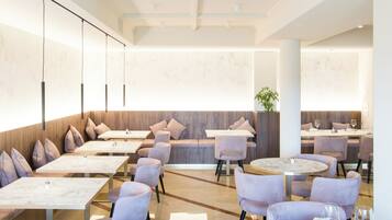 Un restaurant moderne avec des tables surmontées de marbre et des chaises rembourrées, agrémenté d’un mur d’accent en bois et d’une grande plante en pot.