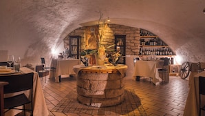 An underground dining area with stone walls, tables, chairs, and a central decorative fountain.