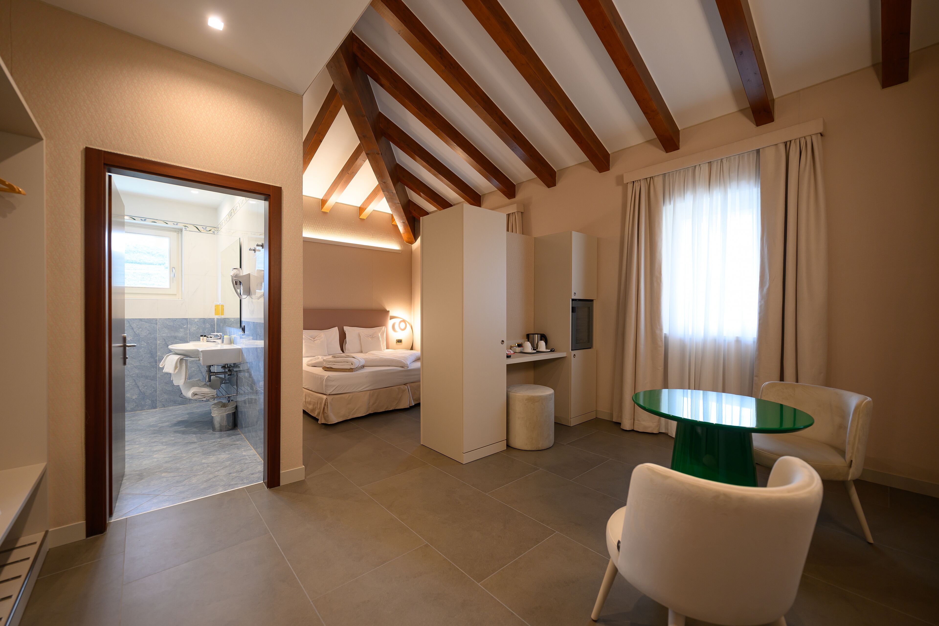 Een moderne hotelkamer met een bed, een badkamer, een zithoek met een tafel en stoelen, en een televisie.