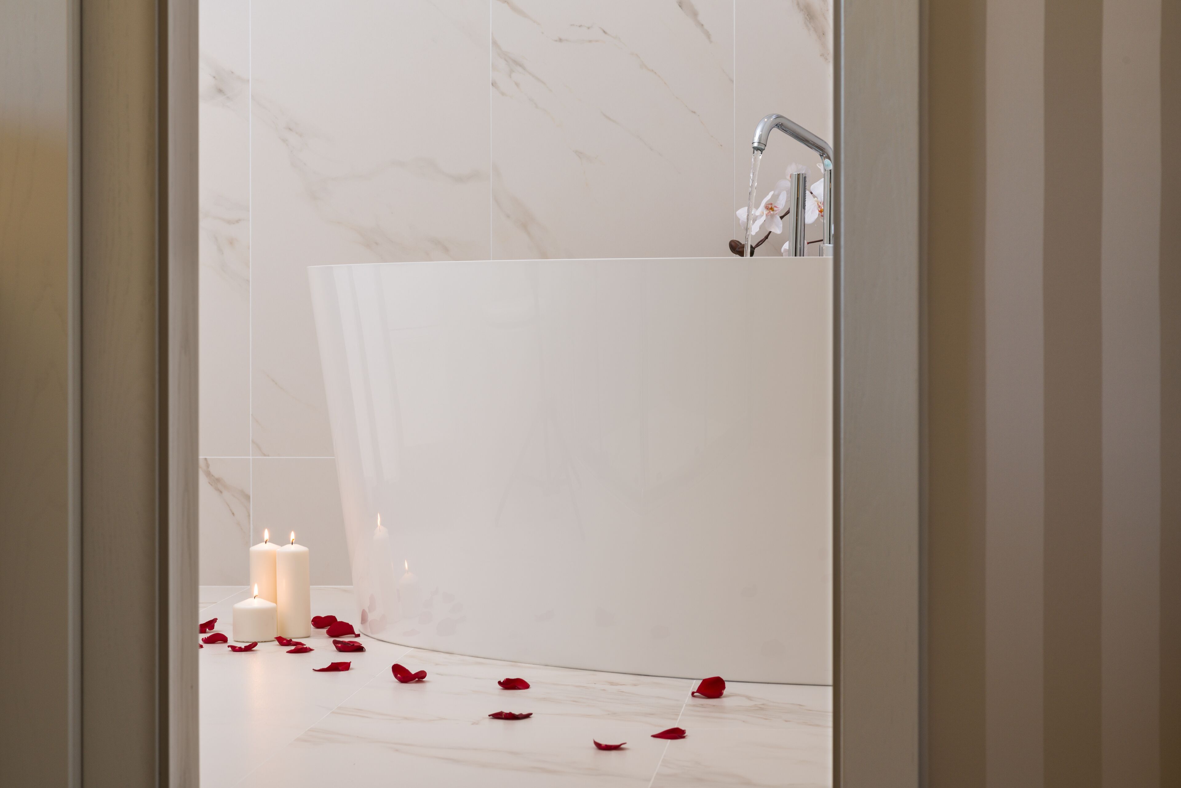 Un baño con suelo de mármol, una bañera blanca y dos velas encendidas.