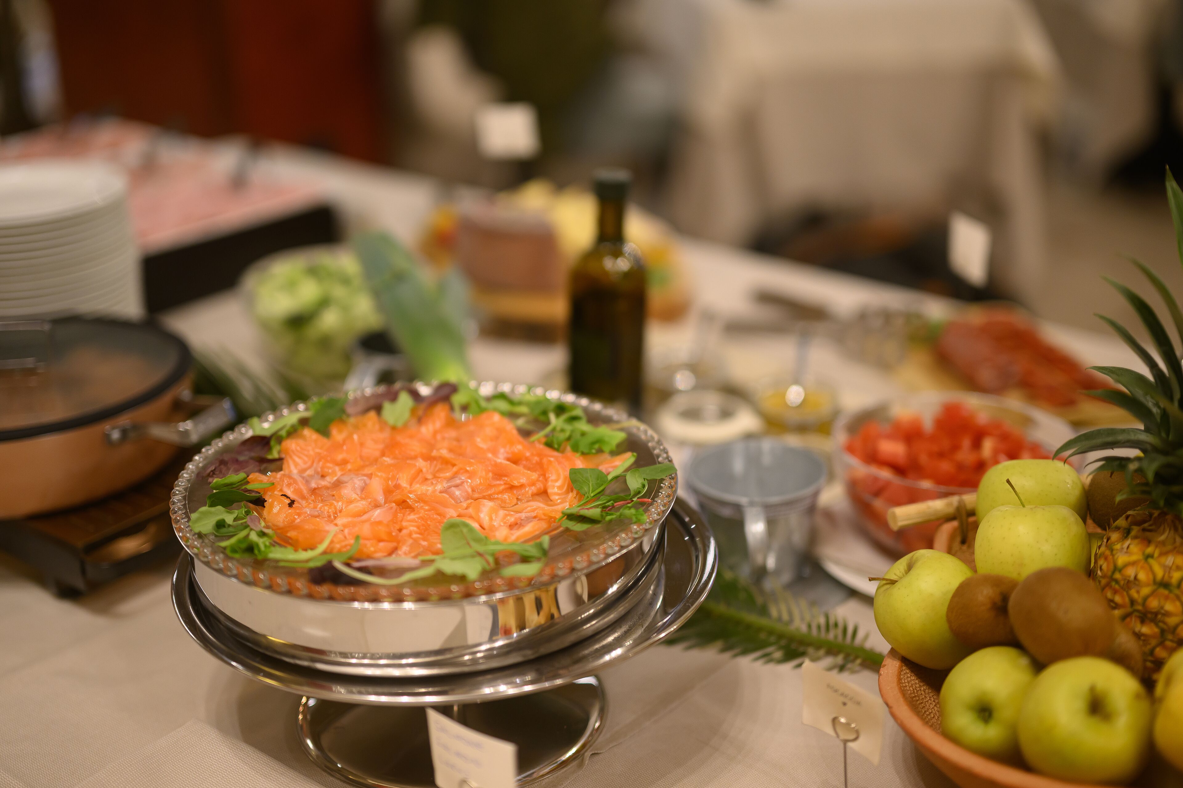 A buffet table with various dishes including salmon, fruits, and a salad.
