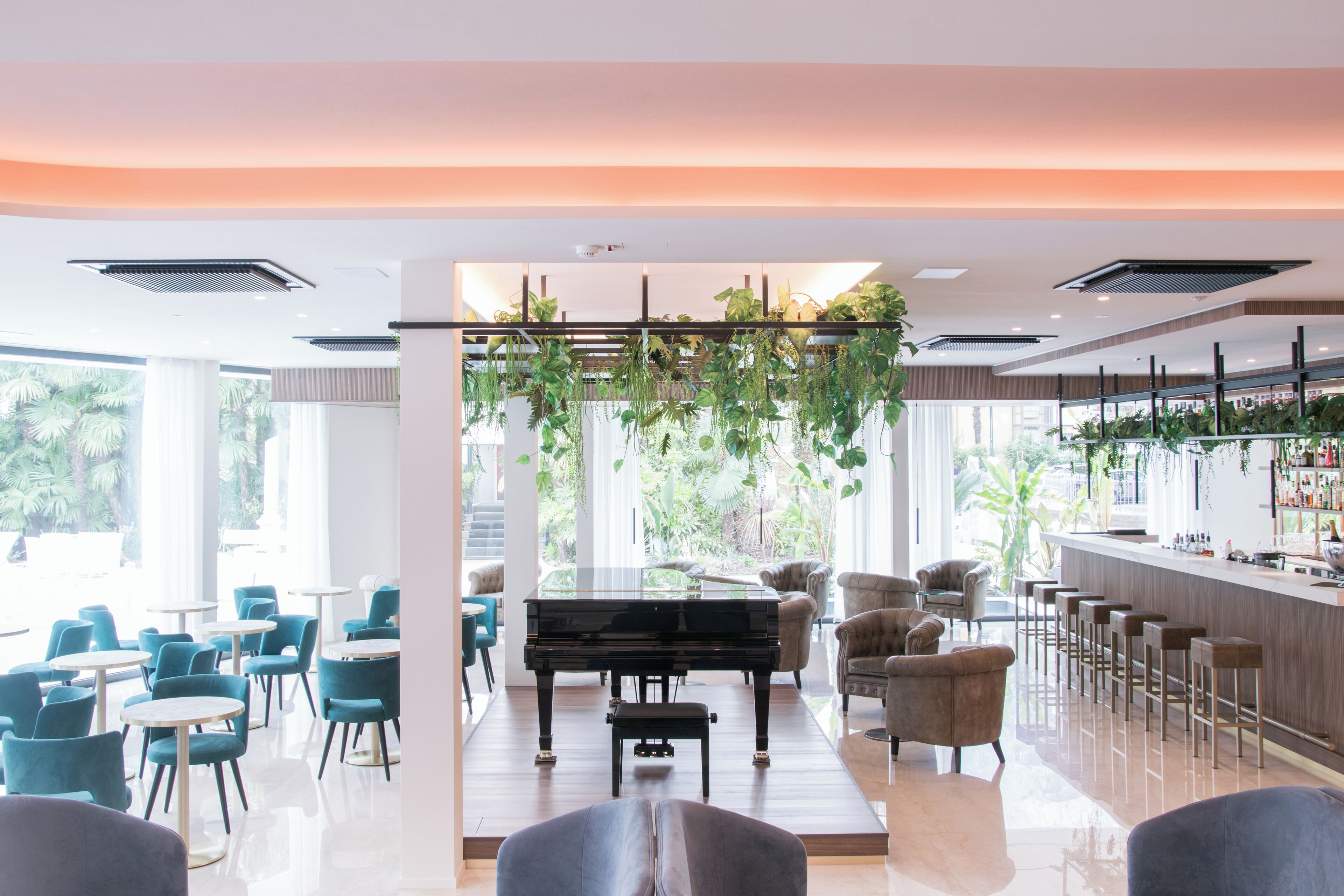A modern lounge area with a grand piano, comfortable seating, a bar, and large windows allowing natural light.
