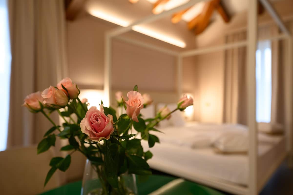 Una habitación de hotel con una cama, un jarrón de rosas rosadas y una mesa verde.