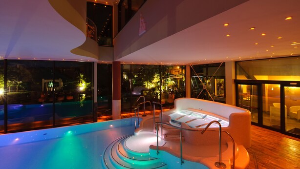 A modern indoor pool area with a curved design, a seating area with a white sofa, and a view of the outside at night.