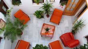 A spacious indoor area with multiple orange chairs and tables, surrounded by potted plants and a wooden door. - La Casa del Duque (Osuna)