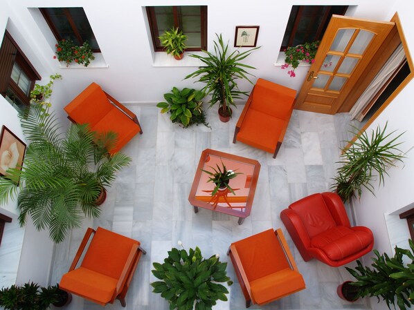 A spacious indoor area with multiple orange chairs and tables, surrounded by potted plants and a wooden door.