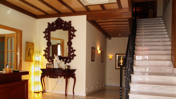 A spacious lobby with a marble floor, a wooden staircase, and a large ornate mirror. - La Casa del Duque (Osuna)