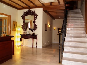 A spacious lobby with a marble floor, a wooden staircase, and a large ornate mirror.