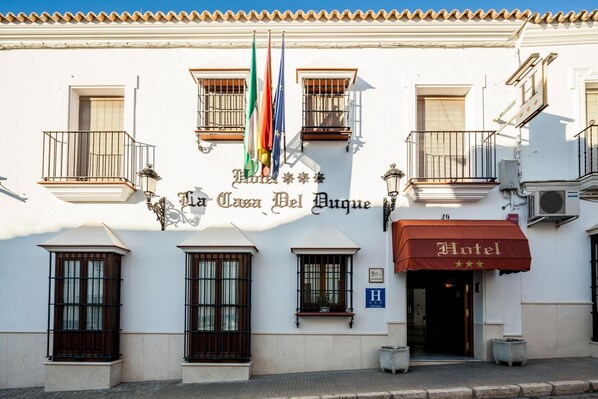A hotel facade with balconies, a sign reading "Hotel La Casa Del Bague", and multiple flags.