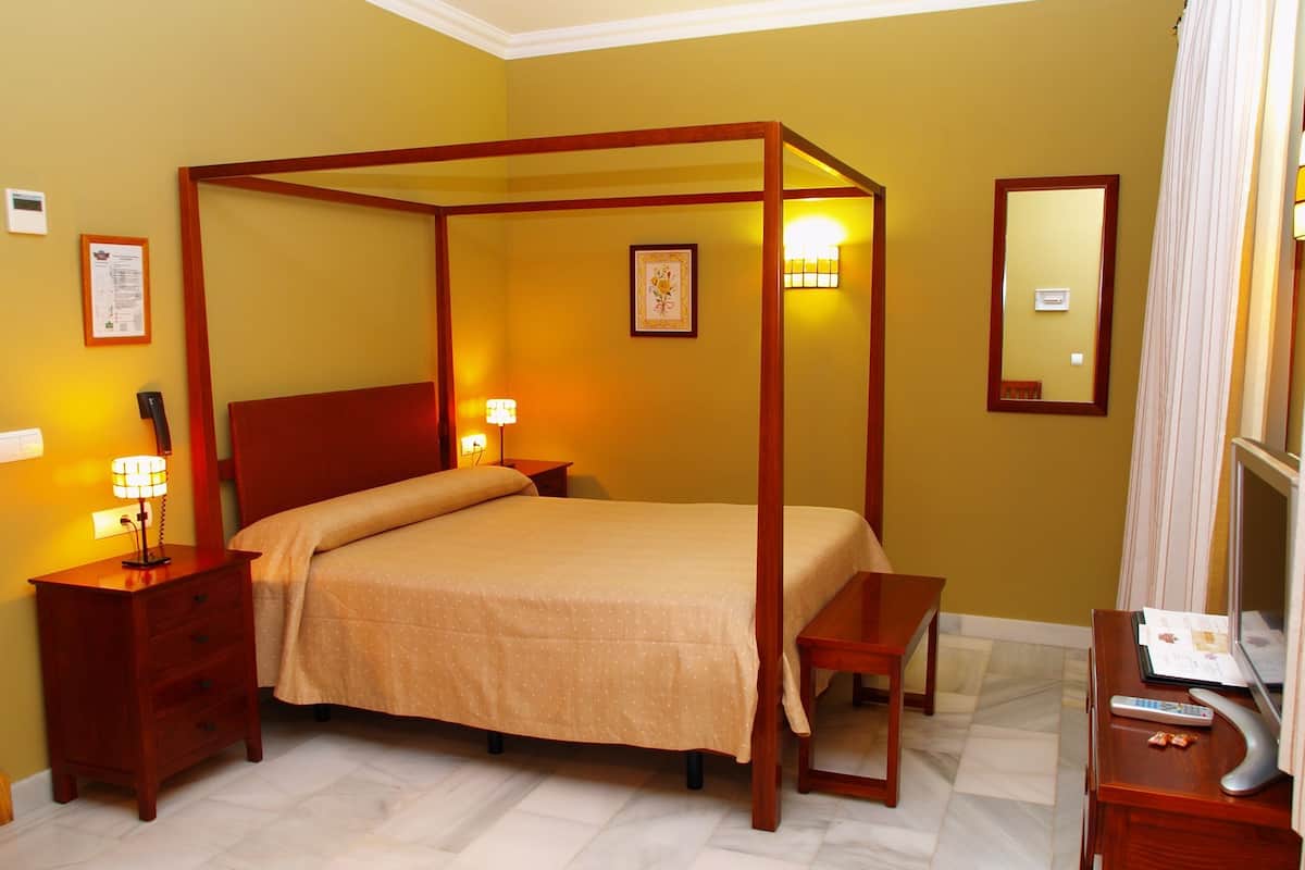 A four-poster bed with a wooden frame, a bedside table with a lamp, a nightstand with a telephone, and a mirror on the wall.