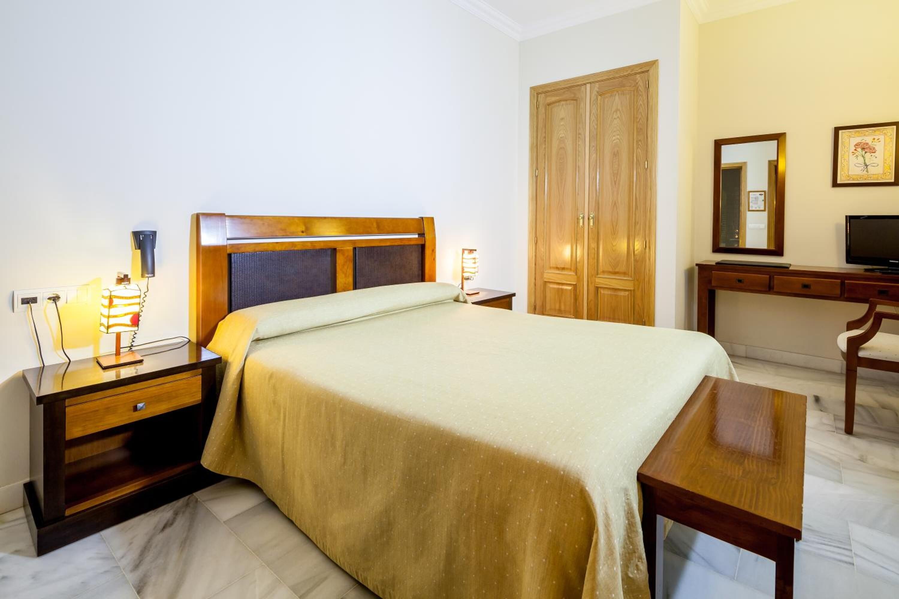 A hotel room with a bed, bedside tables, a wardrobe, a desk with a television, and a mirror.