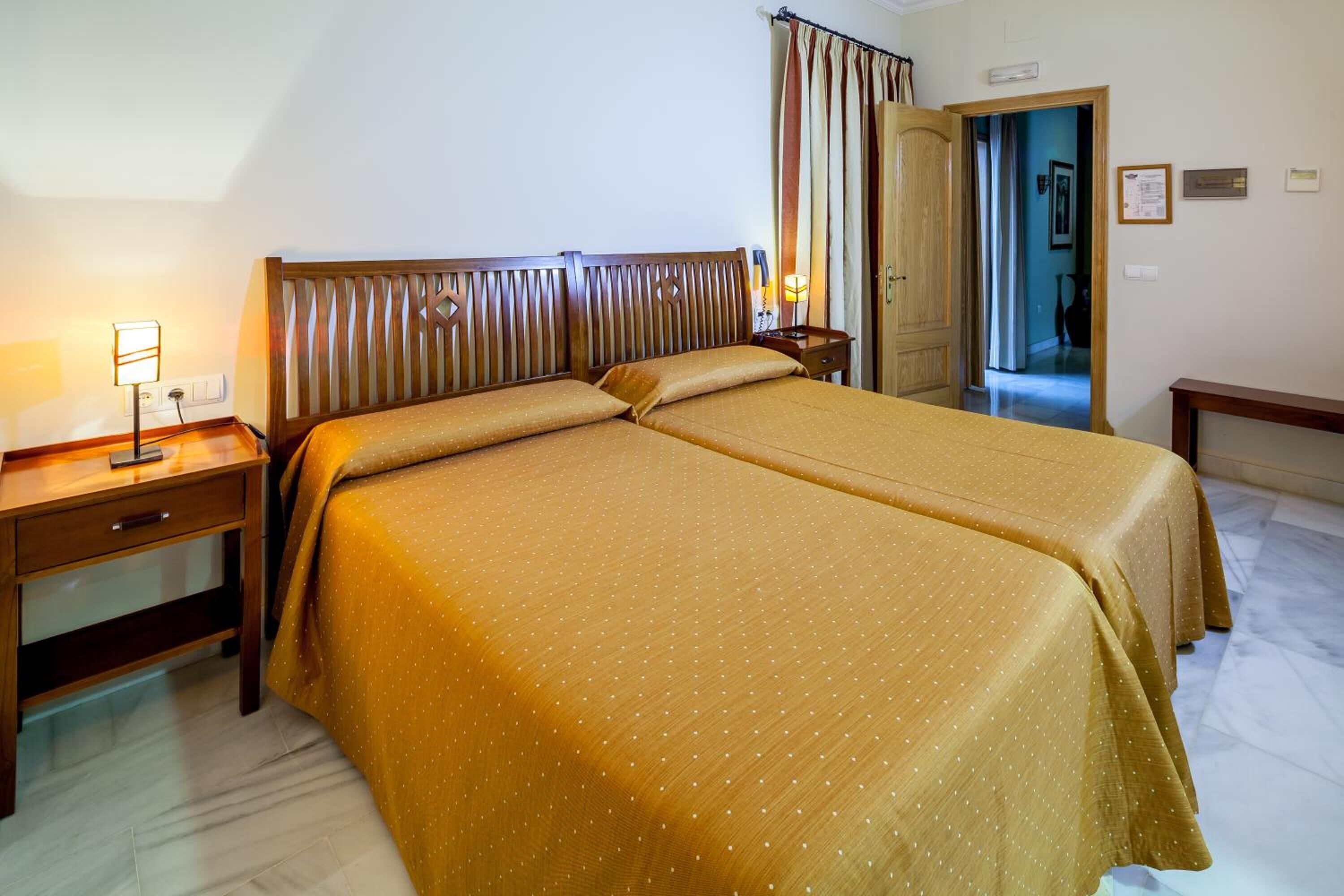 Ein Hotelzimmer mit einem großen Bett, einem Nachttisch mit einer Lampe und einer Tür zu einem weiteren Raum.