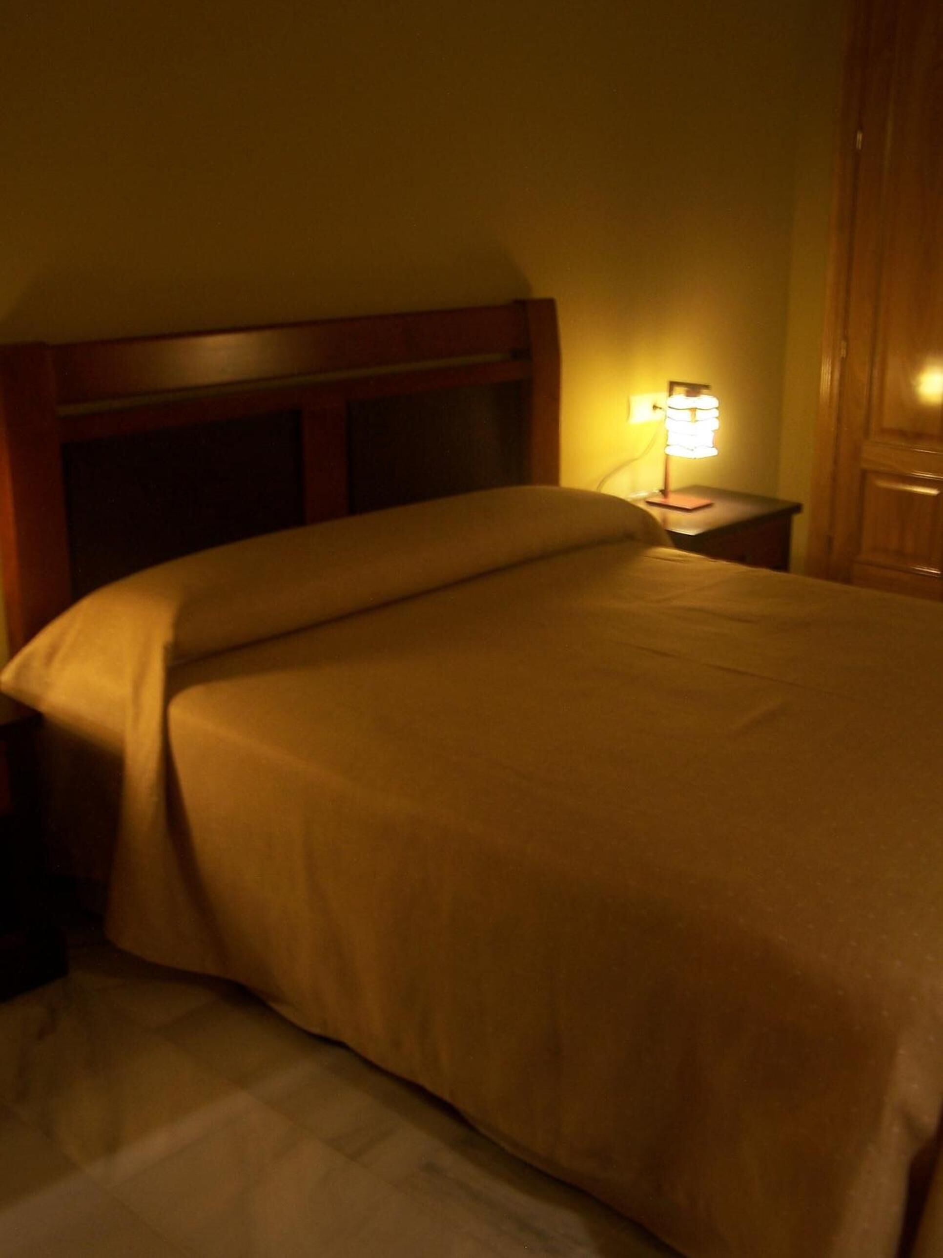 A hotel room with a bed, a nightstand with a lamp, and a wooden headboard.