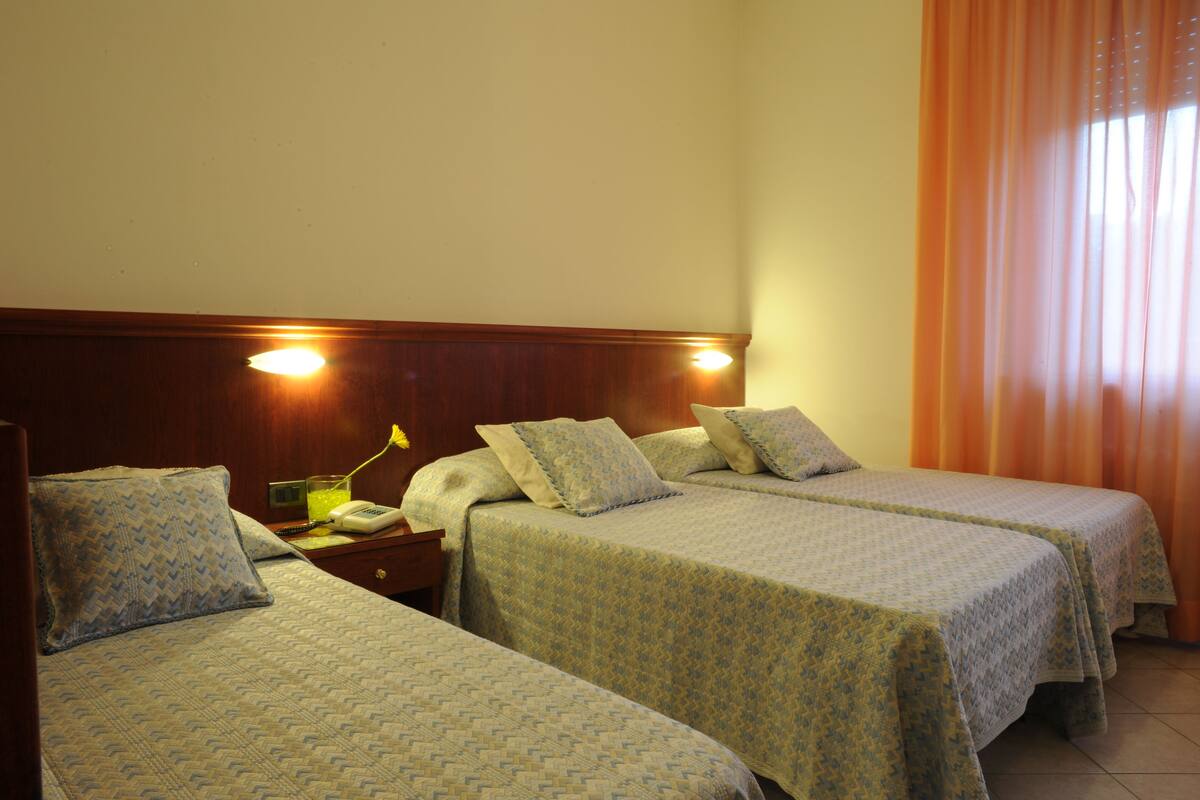A hotel room with two single beds, wooden headboards, and a bedside table with a lamp and phone.
