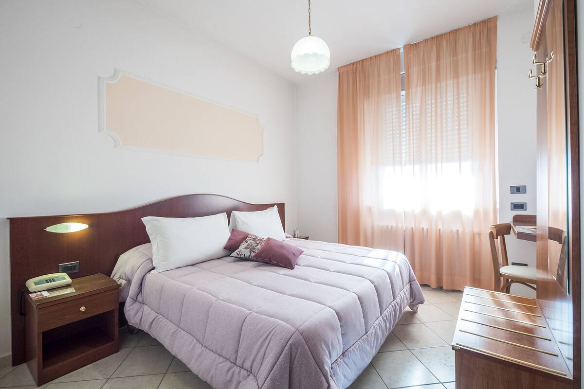 A neatly arranged bedroom with a bed, bedside table, lamp, and a chair.