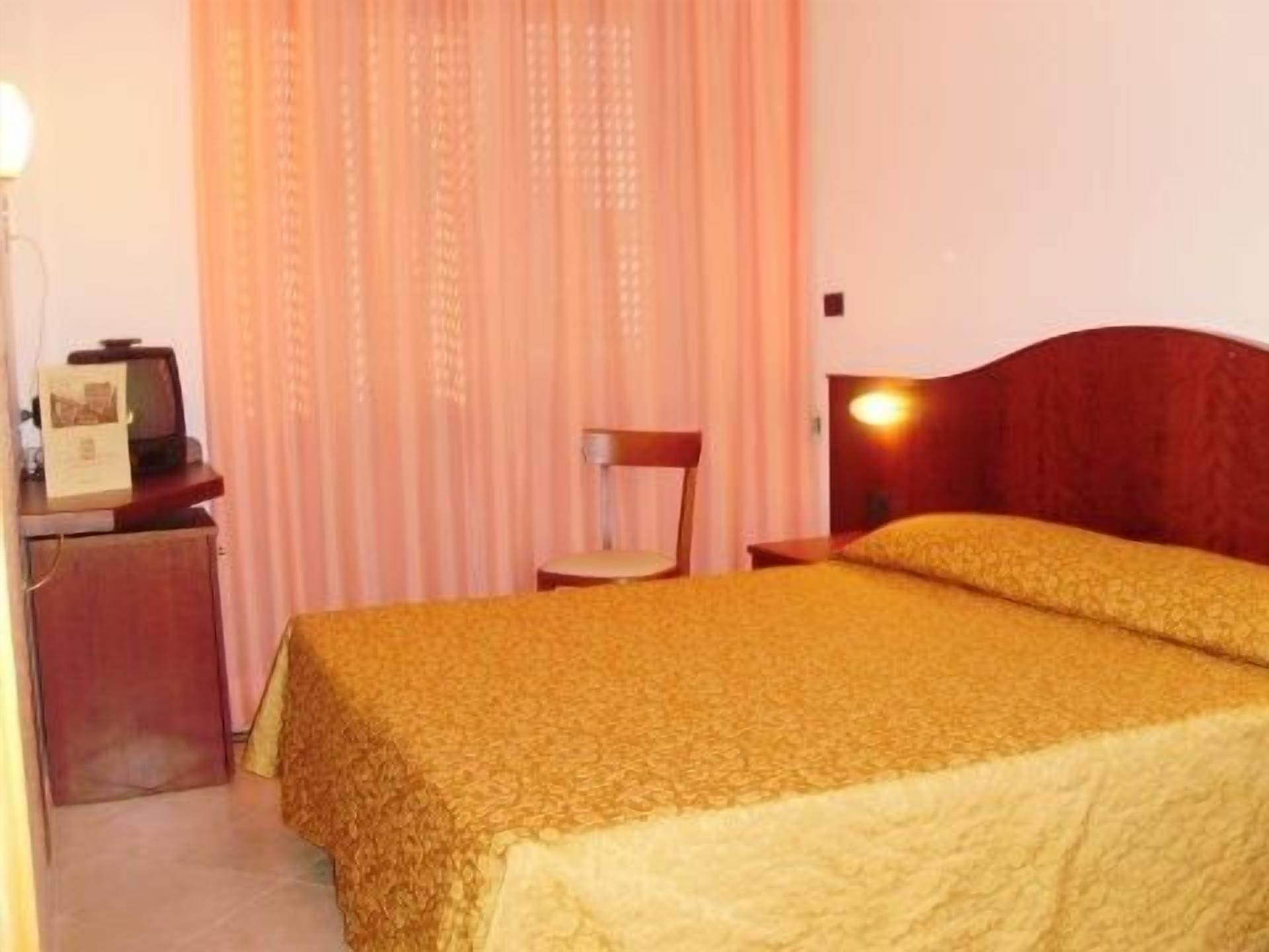 A hotel room with a bed, a desk with a lamp, and a chair.
