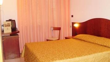 A hotel room with a bed, a desk with a lamp, and a chair.