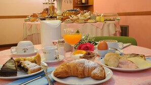 Una mesa de desayuno con cruasanes, bollería, huevos y zumo de naranja.