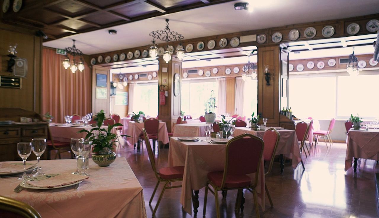 Een eetruimte met tafels gedekt voor meerdere gasten, met een klassiek interieur, houten balken en decoratieve borden aan de wanden.