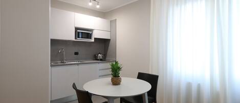 A modern kitchen with a microwave, sink, and cabinets. There is a dining table with chairs and a potted plant.