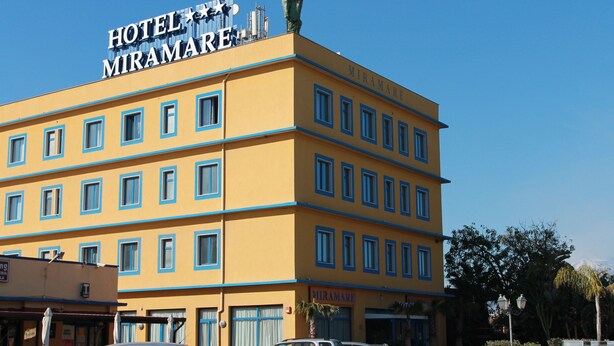 Ein mehrstöckiges Hotel namens MIRAMARE mit einer gelben Fassade und blauen Fensterrahmen.