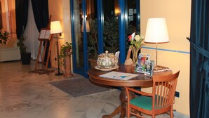 Eine Hotelhalle mit einem runden Holztisch, einem Stuhl, einer Blumenvase, einer Lampe und einer Tür mit blauen Vorhängen.