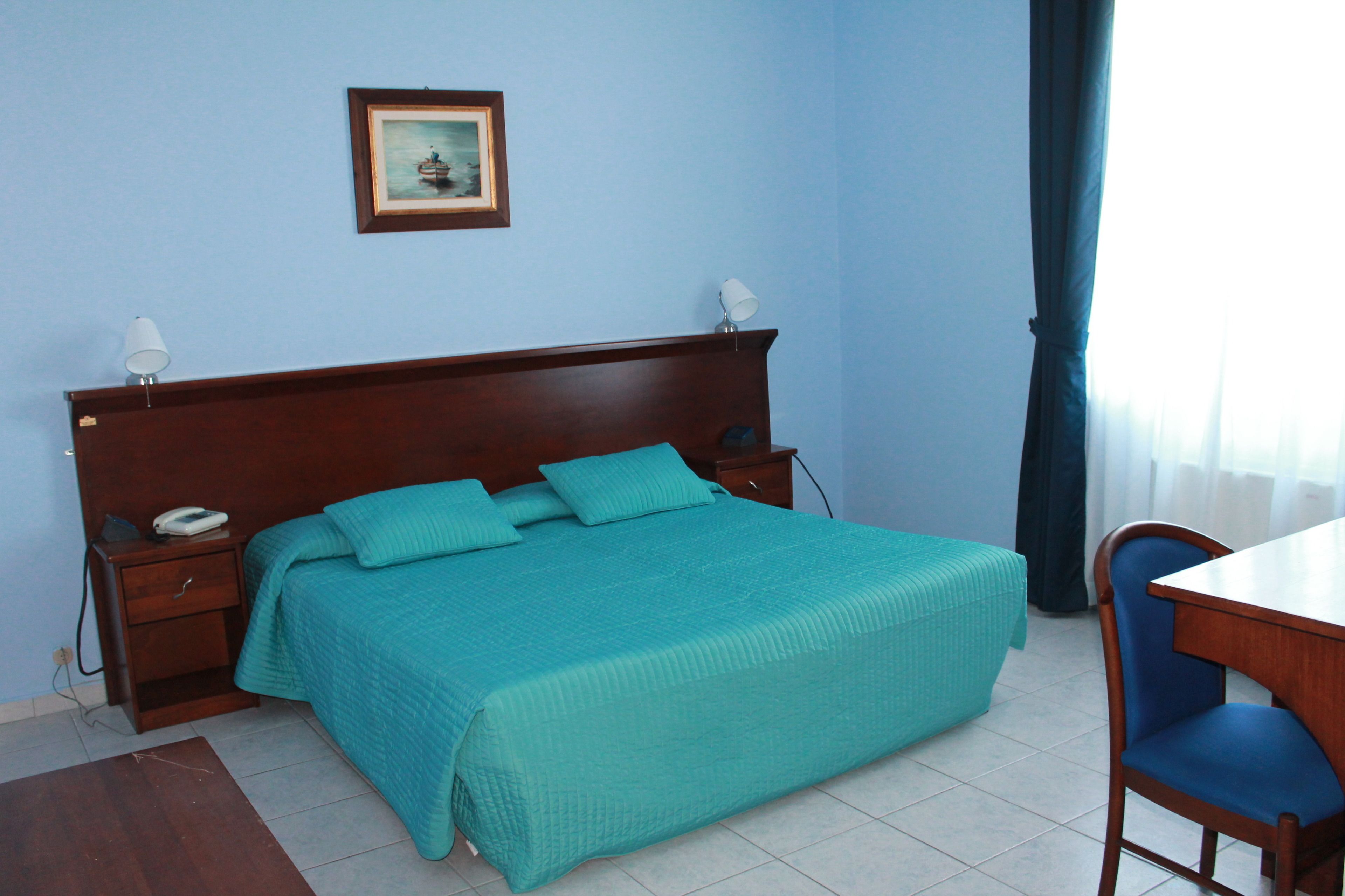 Un dormitorio ordenado con cama, mesitas de noche, una silla e imagen enmarcada en la pared.
