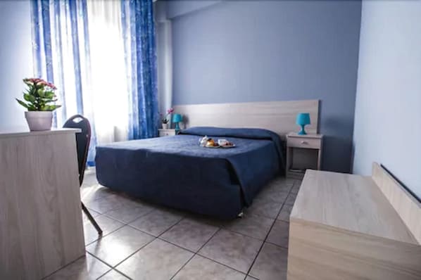 A bedroom with a bed, bedside tables, a desk, and a potted plant.