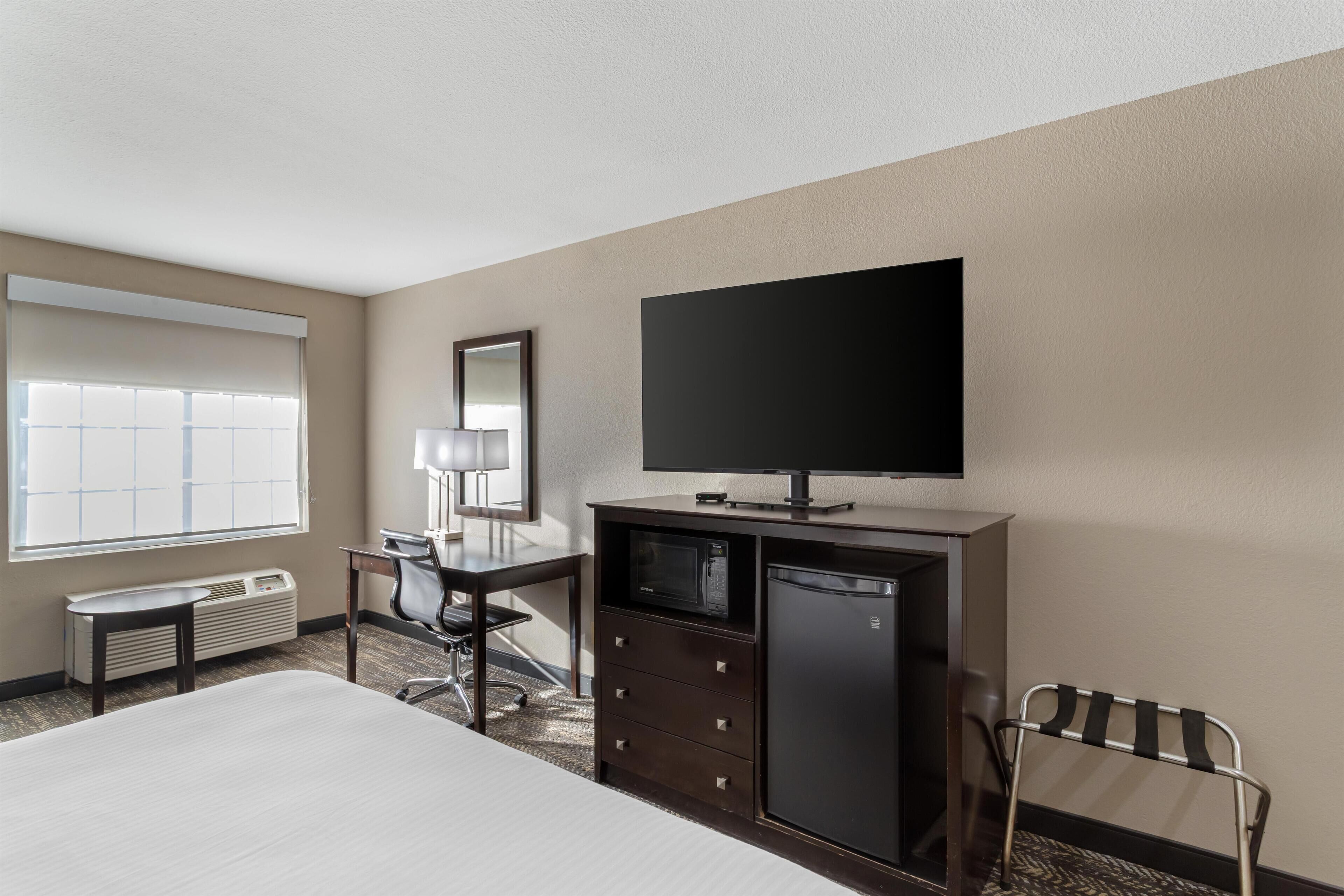A hotel room with a bed, a desk, a chair, a television, a microwave, and a refrigerator.