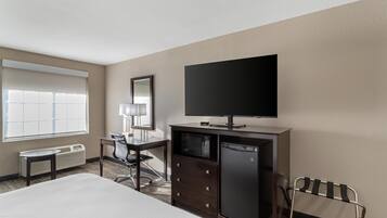 A hotel room with a bed, a desk, a chair, a television, a microwave, and a refrigerator.