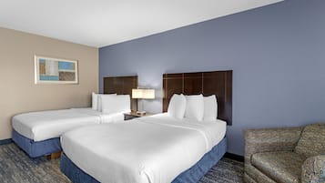 A hotel room with two beds, a nightstand with a lamp, a patterned armchair, and a framed picture on the wall.