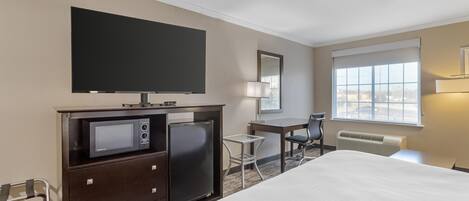 A hotel room with a bed, a desk, a chair, a TV, a microwave, and a refrigerator.