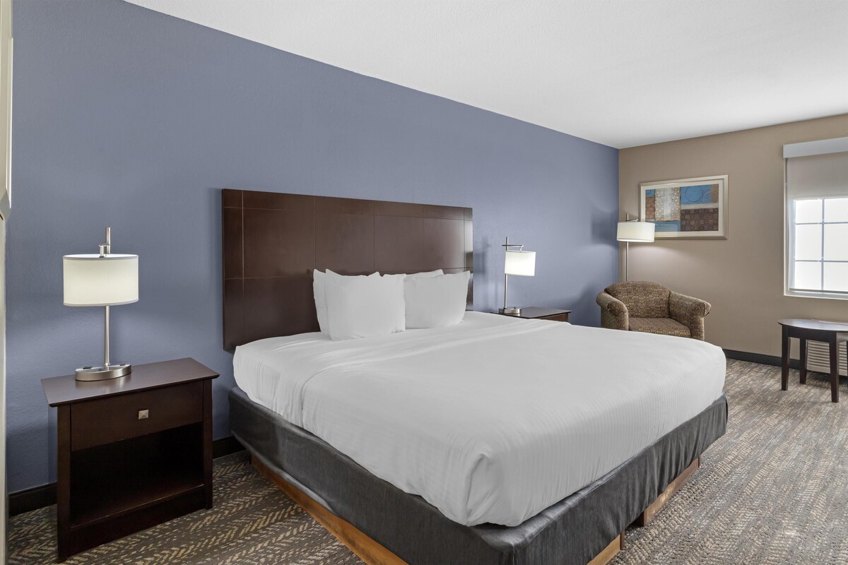 A hotel room with a large bed, two bedside tables with lamps, a chair, and a small table.