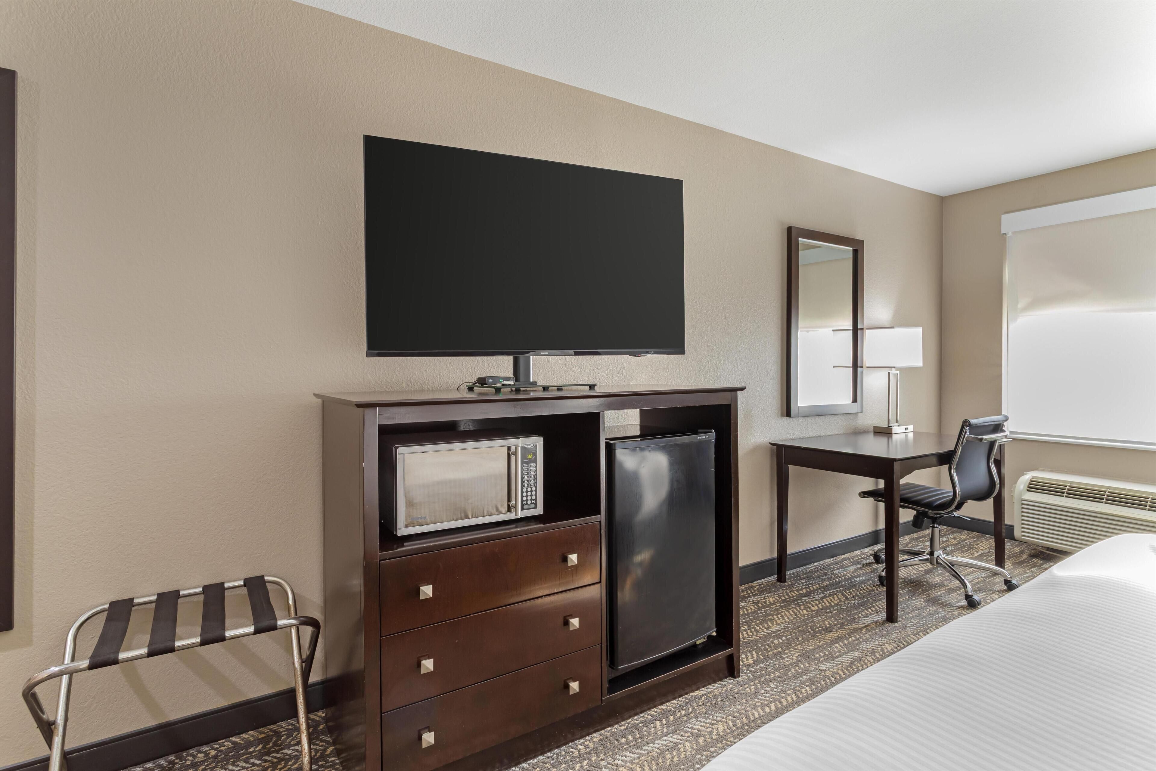 Habitación de hotel con cama, escritorio con computadora, microondas, refrigerador, televisor, silla y ventana con vista.