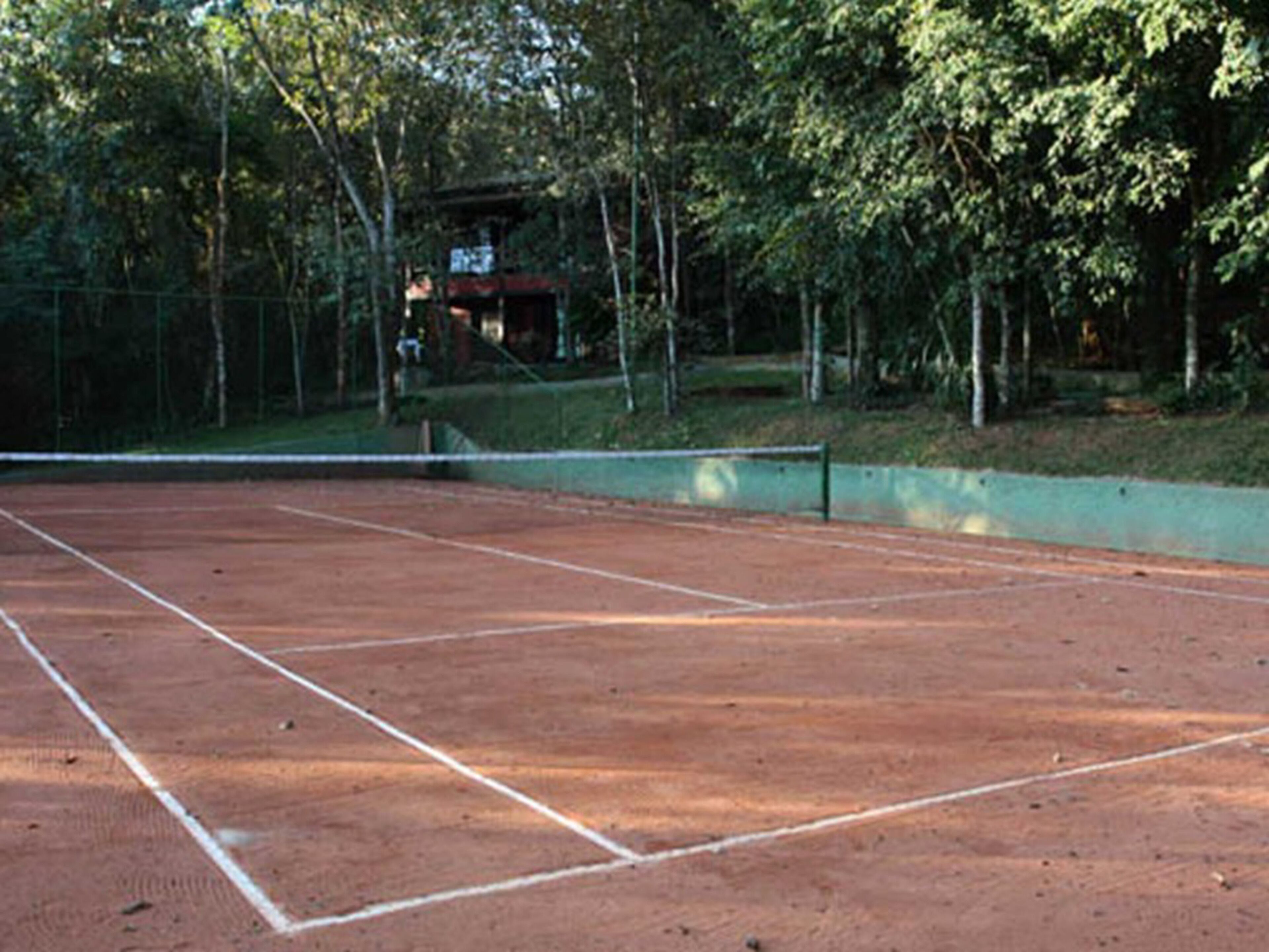 Cancha de tenis con red, rodeada de árboles y una valla.