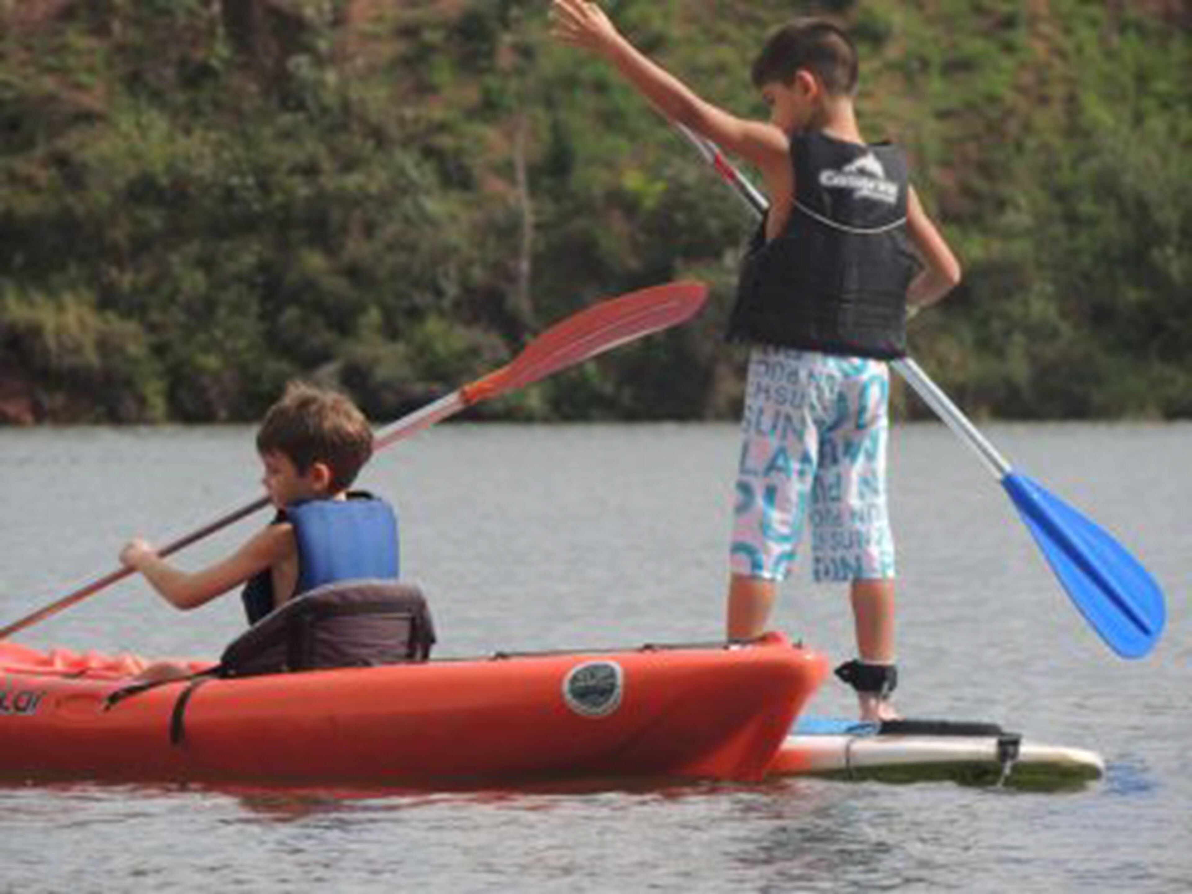 Two individuals in a small, orange inflatable boat on a body of water.