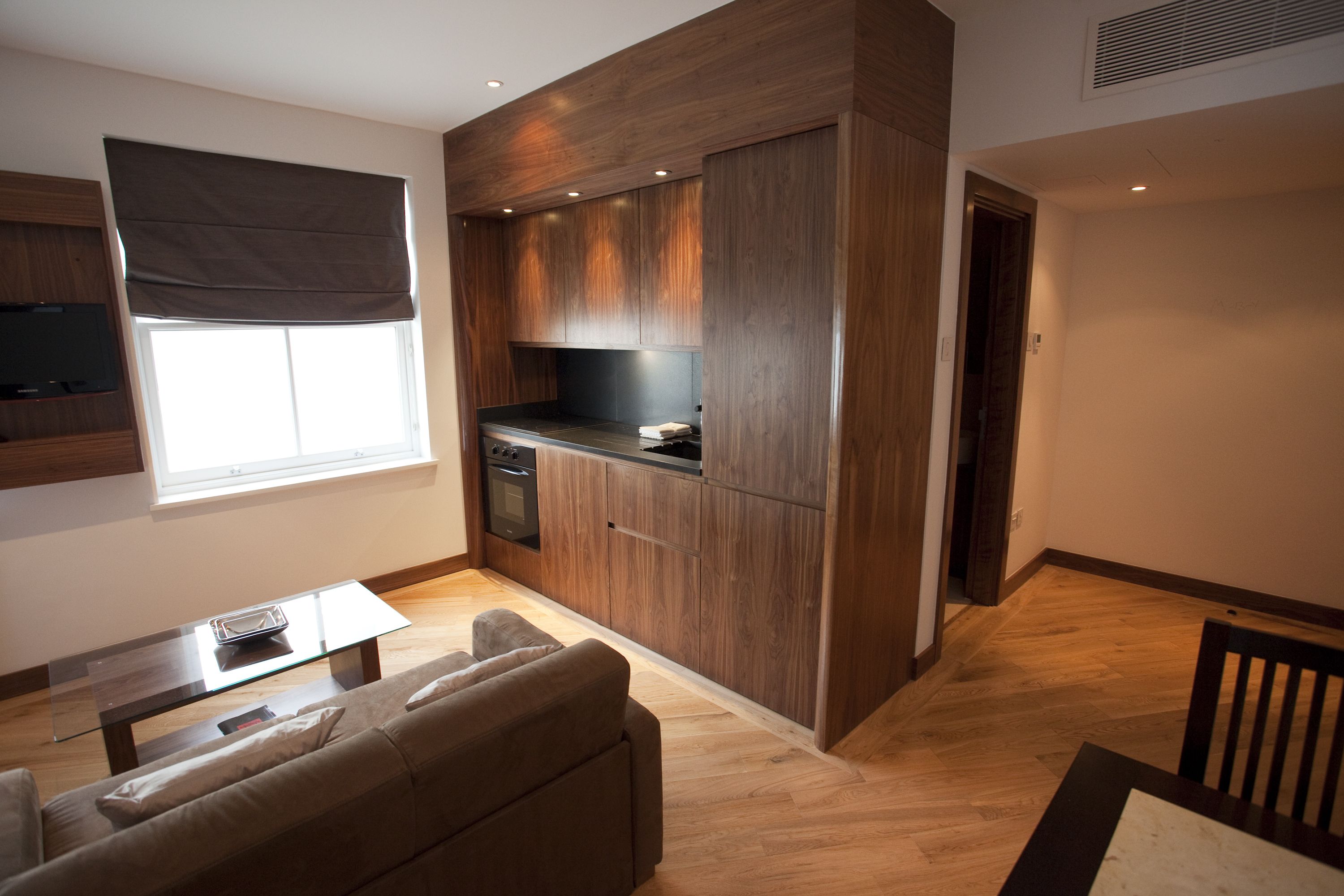 A modern kitchen with wooden cabinets, a built-in oven, and a dining area with a glass table and sofa.