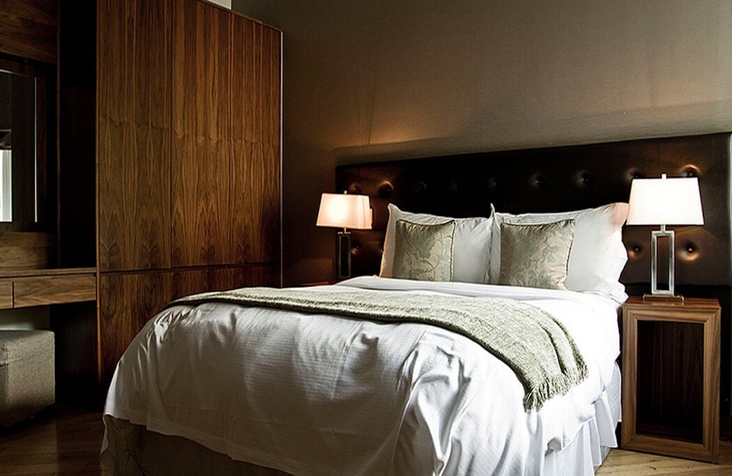 A hotel room with a large bed, two bedside lamps, and a wooden wardrobe.