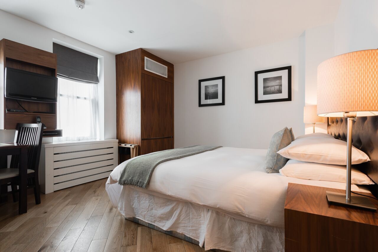 A bedroom with a bed, bedside table, lamp, TV, and a desk with chair.