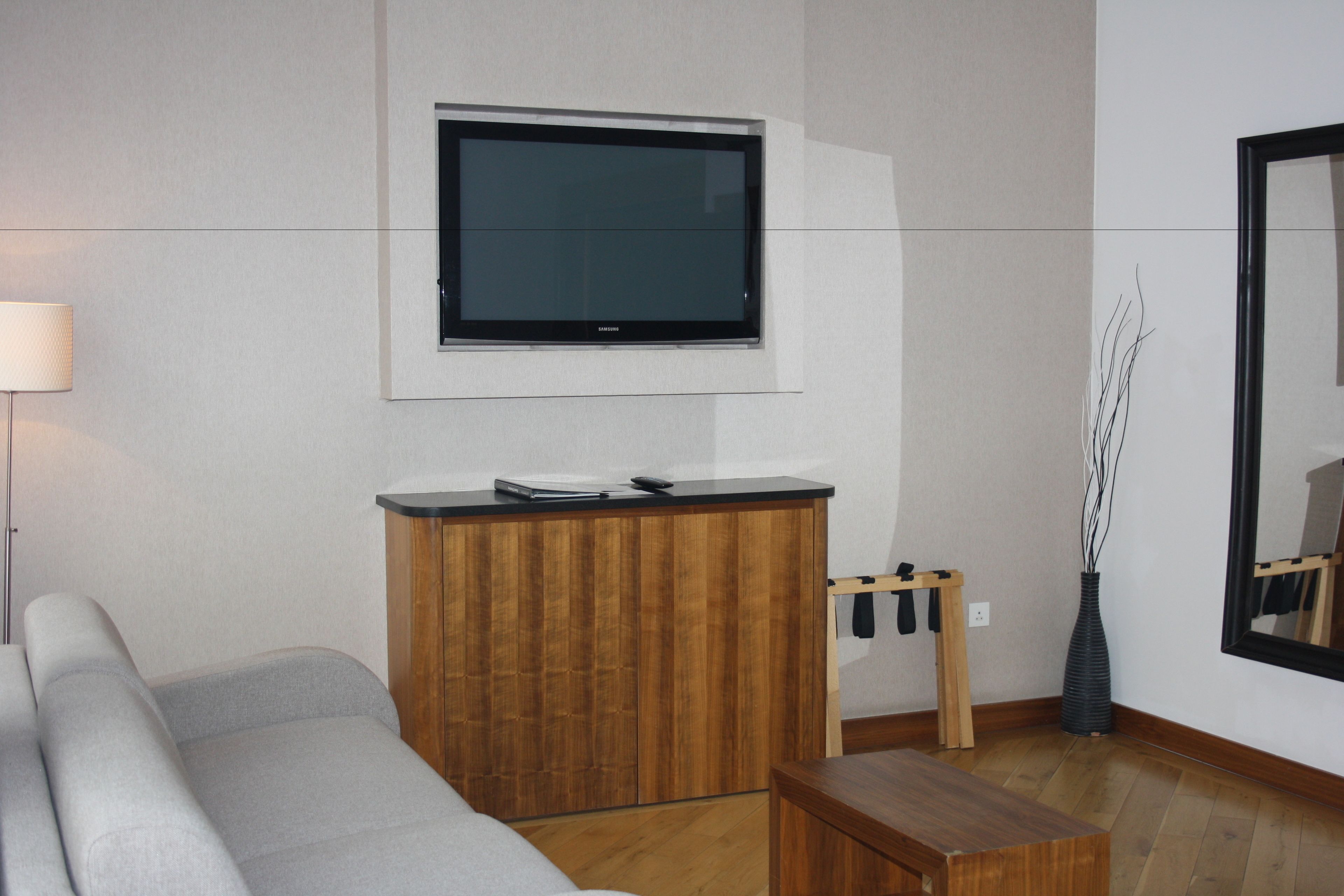 A modern living room with a grey sofa, wooden cabinet, and a mounted flat-screen TV.