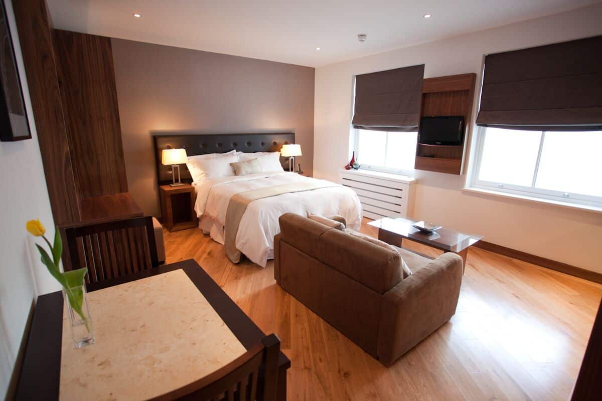 A modern hotel room with a large bed, a sofa, a small table, and a TV mounted on the wall.