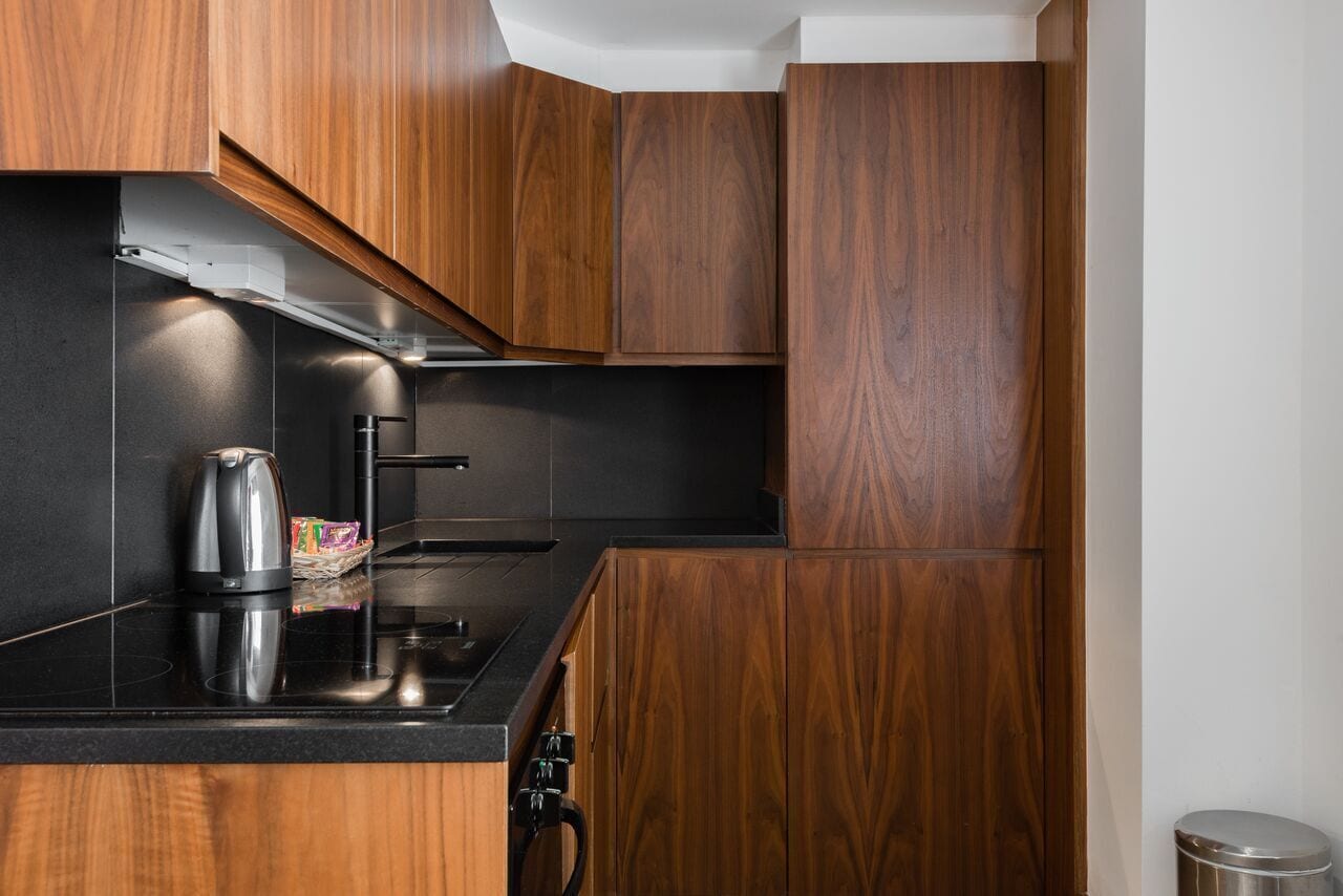 A modern kitchen with wooden cabinets, a black countertop, a kettle, and a stainless steel range hood.