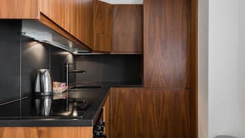 A modern kitchen with wooden cabinets, a black countertop, a kettle, and a stainless steel range hood.