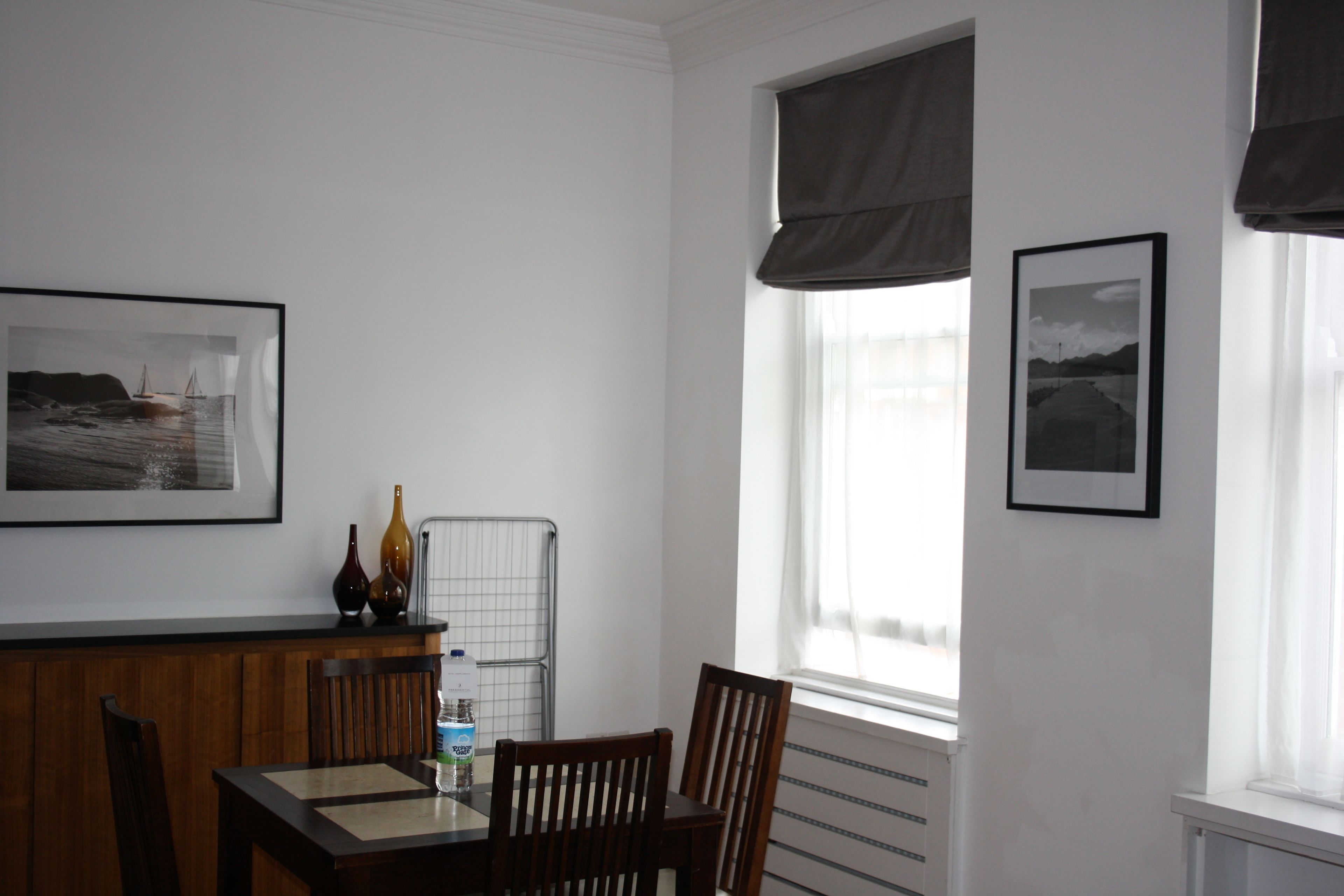 A dining area with a wooden table and chairs, a water bottle, and two framed pictures on the wall.